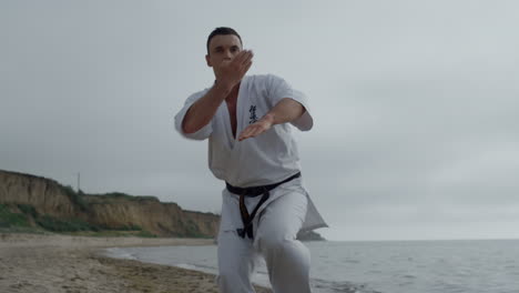 un luchador de karate entrenando ejercicios de lucha en la playa. un hombre practicando artes marciales.