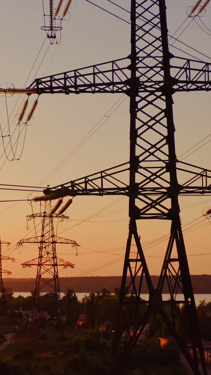 Transmission lines near the river. High-voltage electric towers at sunset. Distribution and supply of electricity. Camera rising up. Vertical video