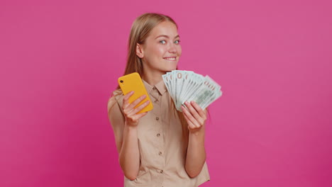 young woman use smartphone rejoicing win, receiving money dollar cash banknotes, celebrating success