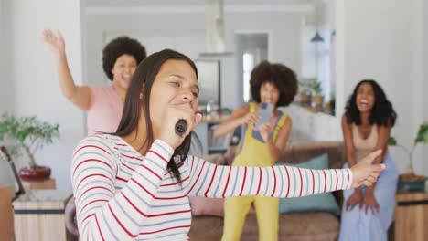 happy diverse female friends singing into microphone in living room