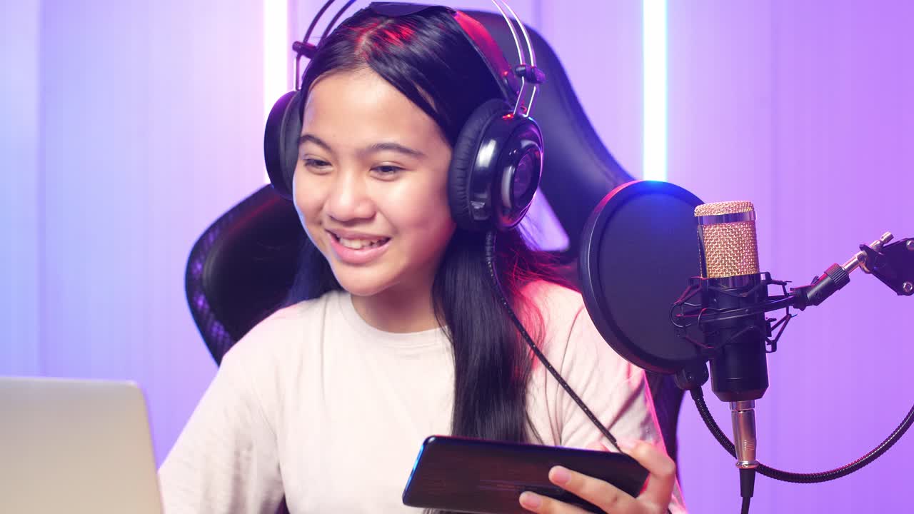 Asian Kid Girl Holding Mobile Phone And Read Comment In Laptop Computer Then Talking To Camera While Live Stream