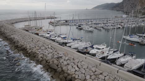 convoy of dark coloured cars driving across long wealthy yacht marina harbour aerial tracking orbit left