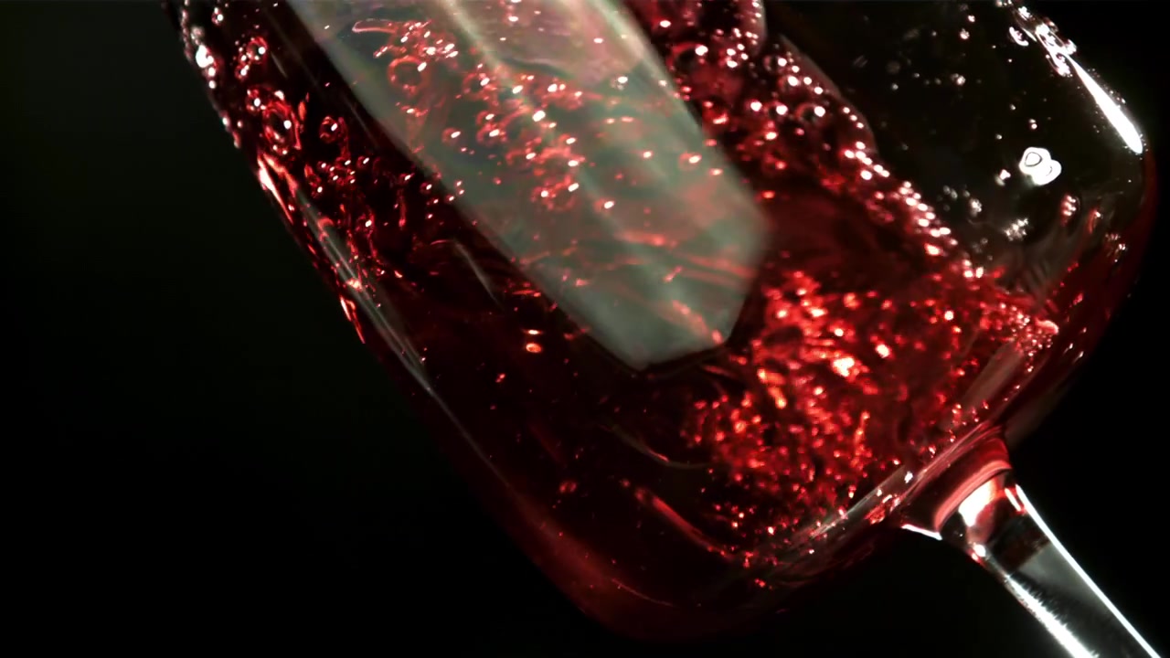 Vino rosso versato al rallentatore in un bicchiere con bollicine.