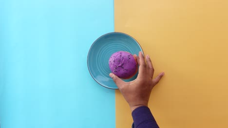 closeup of a hand reaching for a purple donut on a blue plate