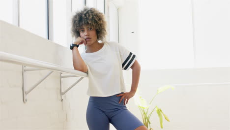 Biracial-young-woman-leaning-on-ballet-barre,-wearing-sportswear