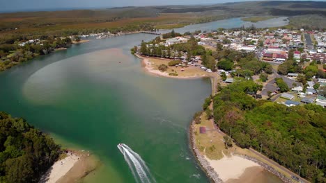 aerial view of a boat on a river and the evans head town, new south wales, australia - tilt up, drone shot