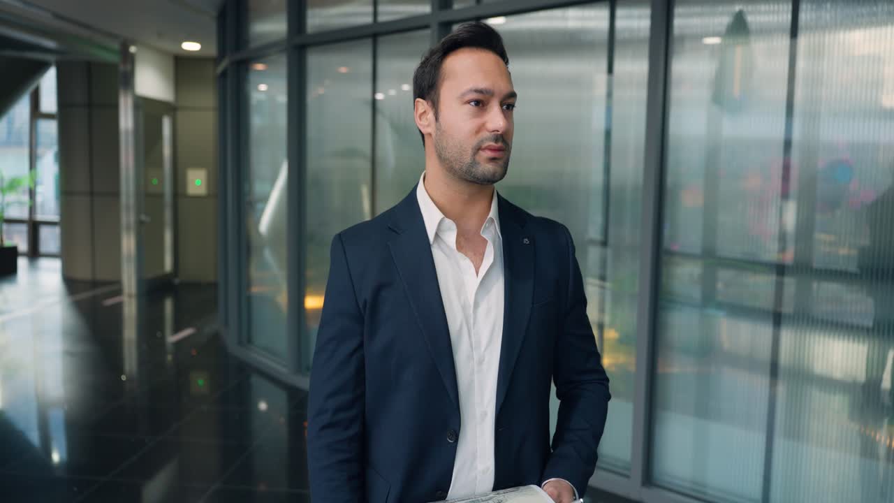 Frustreret mandlig direktør i mørkt jakkesæt står i en moderne kontorkorridor med glasvægge og gennemgår dokumenter med et fortvivlet udtryk over dårlige økonomiske resultater - slow motion