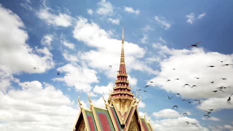 Pájaros-Volando-Hacia-La-Libertad-En-Cámara-Lenta-Alrededor-De-La-Pacífica-Aguja-De-La-Pagoda-Budista-Con-Un-Hermoso-Cielo-Azul-Y-Nubes-Esponjosas,-Un-Dron-Lento-Y-Simple-Gira-En-órbita