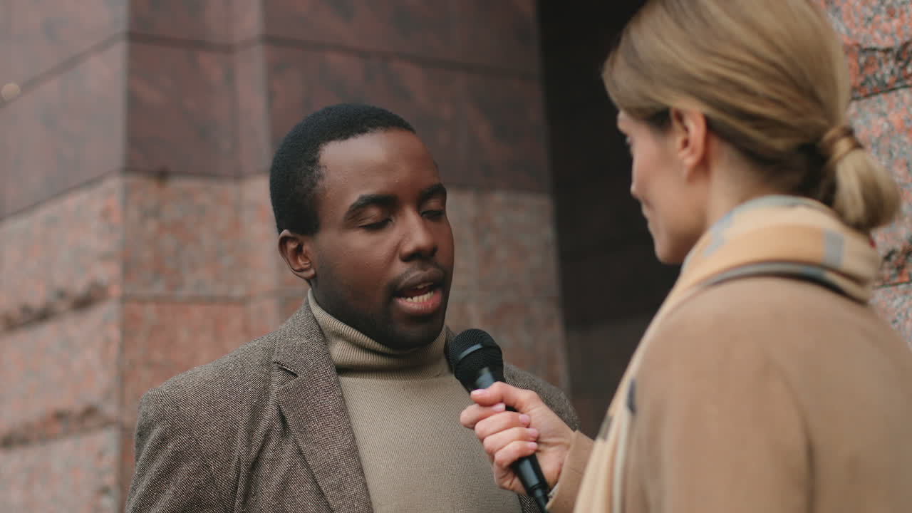 vista cercana de un hombre afroamericano hablando y respondiendo a una periodista en la calle en otoño