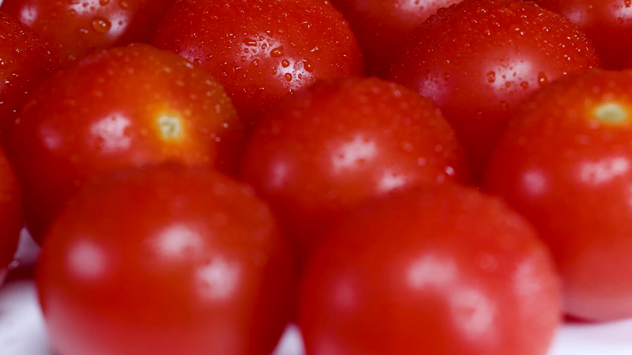 Macro video of cherry tomatoes rotating under bright lighting, highlighting their vibrant red color and smooth texture