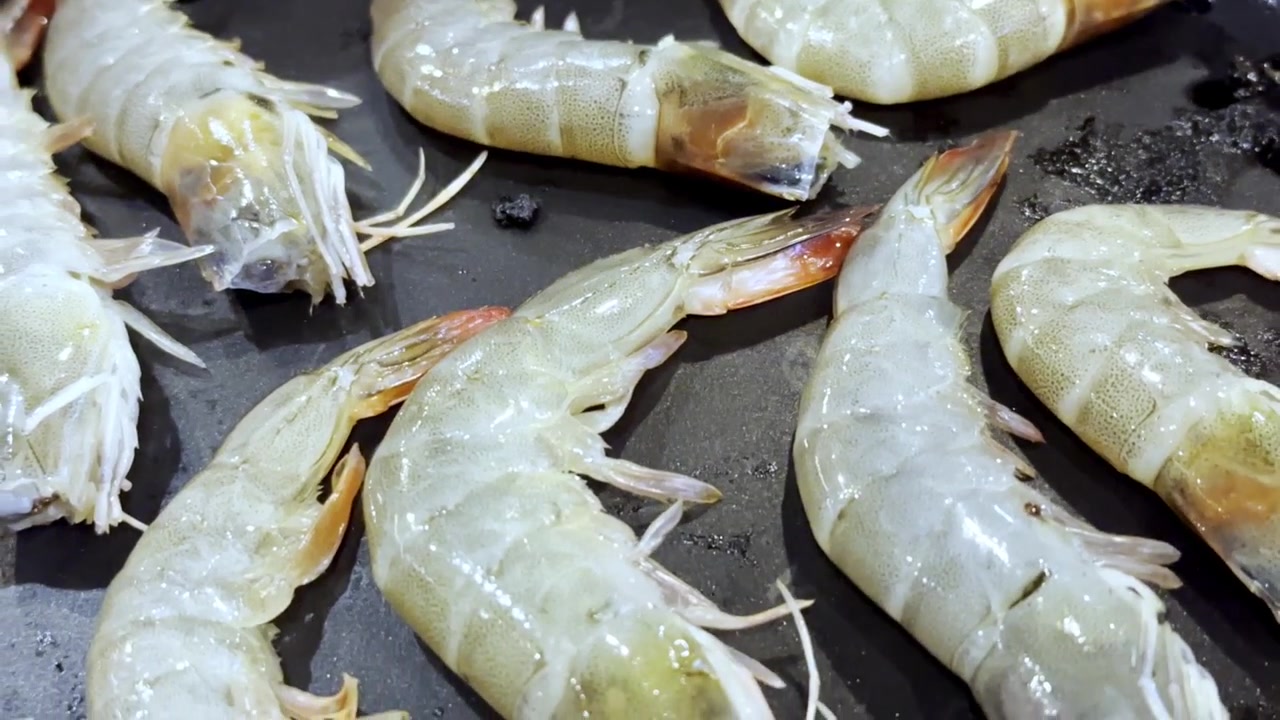 Primo piano di gamberi freschi che sfrigolano su una padella calda da barbecue, catturando frutti di mare succosi, vapore che sale e deliziosi sapori grigliati in una scena di cucina.