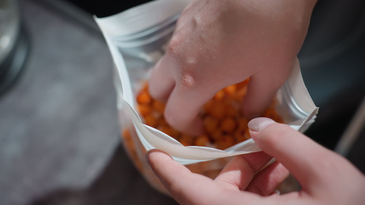 Berry Snack Preparation, Person Selecting Frozen Orange Berries From Resealable Bag In Kitchen, Closeup Of Hand Reaching Into Resealable Pouch Containing Frozen Orange Berries Near Kitchen Counter