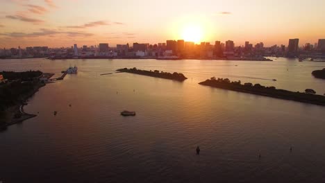 Sunset Over Tokyo Skyline And Tokyo Bay With Cruising Boats Near Bird Island In Odaiba Marine Park, Tokyo, Japan. - aerial