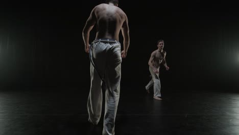 group of a professional dancers are practicing capoeira in darkness against a spotlight on a black background of studio. afro-brazilian martial art that combine elements of dance.