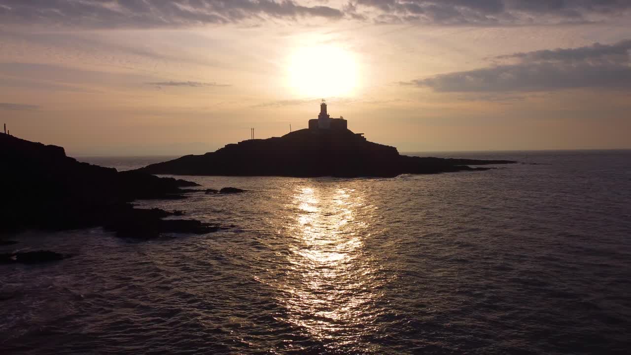 Silhueta do Farol de Mumbles ao Nascer do Sol. Reflexo Dourado do Sol no Oceano com Nuvens Dinâmicas. Perfeito para turismo, documentários de viagem. País de Gales, Reino Unido. 4K