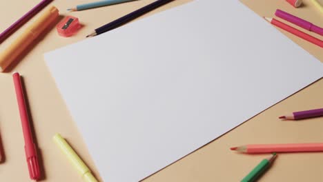 overhead view of blank sheet of paper with school stationery on beige background, in slow motion