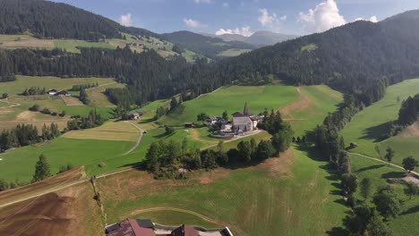 drone pulls back over green land near chiesa di santa maddalena, with three peaks in the dolomites, south tyrol, italy