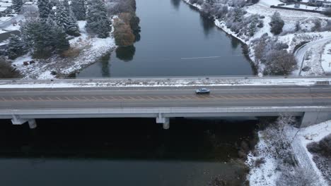 aerial view of a car driving across a bridge with snow covering the ground