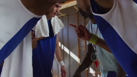 diverse male basketball team and coach in huddle discussing game tactics