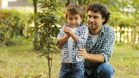 closeup. portrait of a little boy and his dad planting a tree. they laugh and look into the camera. blurred background