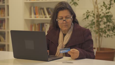 anciana sentada en la mesa con una laptop y comprando productos en línea con tarjeta de crédito