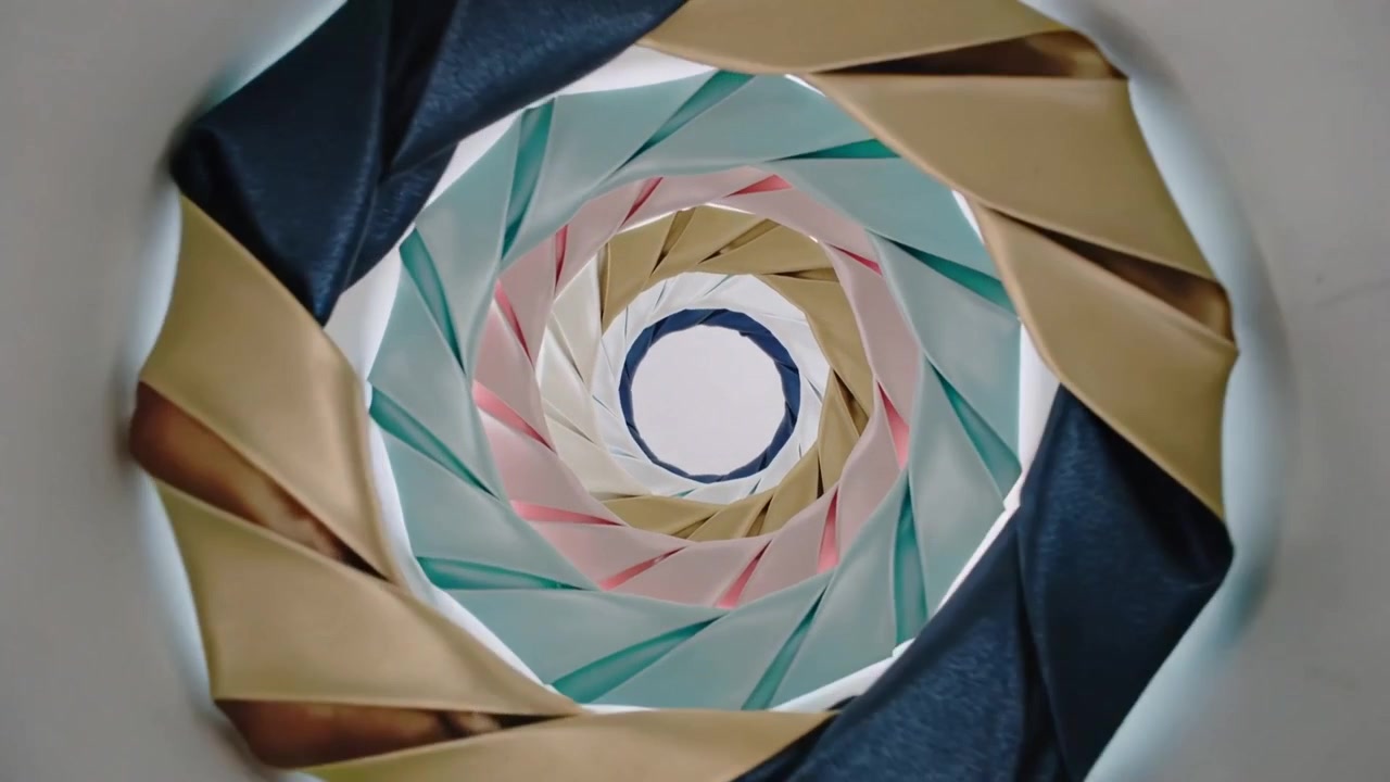 La telecamera zooma verso una spirale piegata all'interno di un tubo di cartone, rivelando pieghe di carta colorata.