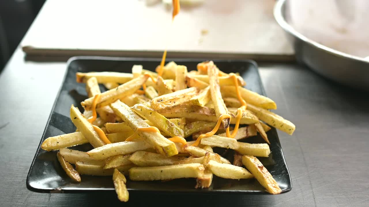 cocinero irreconocible añadiendo salsa de queso en papas fritas
