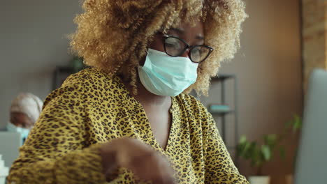 mujer afroamericana con máscara trabajando en la oficina durante la pandemia