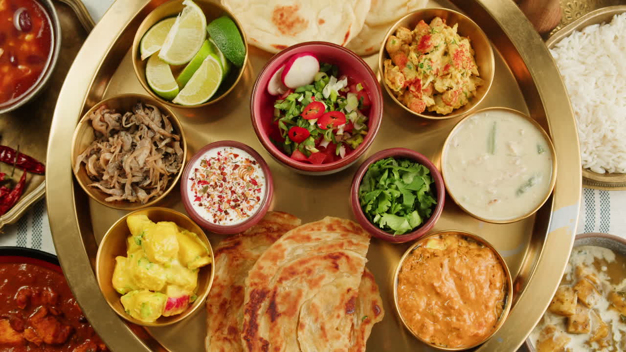 Assorted indian sri-lanka food set on wooden background. Dishes and appetisers of indeed cuisine, rice, lentils, paneer, samosa, spices, masala. Bowls and plates with indian food top view chicken. High quality 4k footage