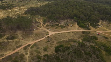 Aerial-tracking-shot-of-vehicle-driving-by-rural-sandy-off-road-beside-forest-trees-near-Punta-del-Diablo-in-Uruguay-during-sunlight