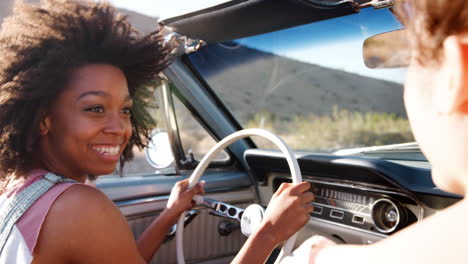 two female friends driving in an open top car, close up