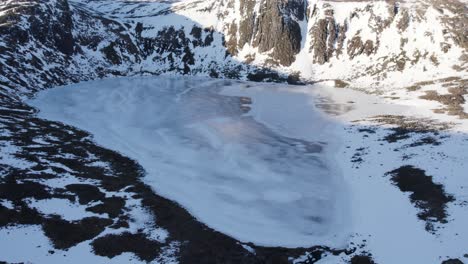 altas imágenes de drones aéreos que vuelan sobre un hermoso lago congelado etchachan, hacia una espectacular e imponente roca cubierta de hielo y un acantilado con empinados barrancos llenos de nieve