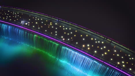 Aerial-top-down-view-turning-clockwise-over-Starlight-Bridge-or-Anh-Sao-Bridge-at-night,-a-pedestrian-bridge-with-colored-lights-and-waterfall-in-District-7-of-Ho-Chi-Minh-City-or-Saigon,-Vietnam