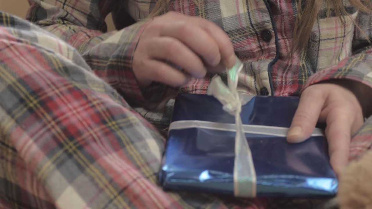 Woman in pajamas opening gift wrapped in paper close up