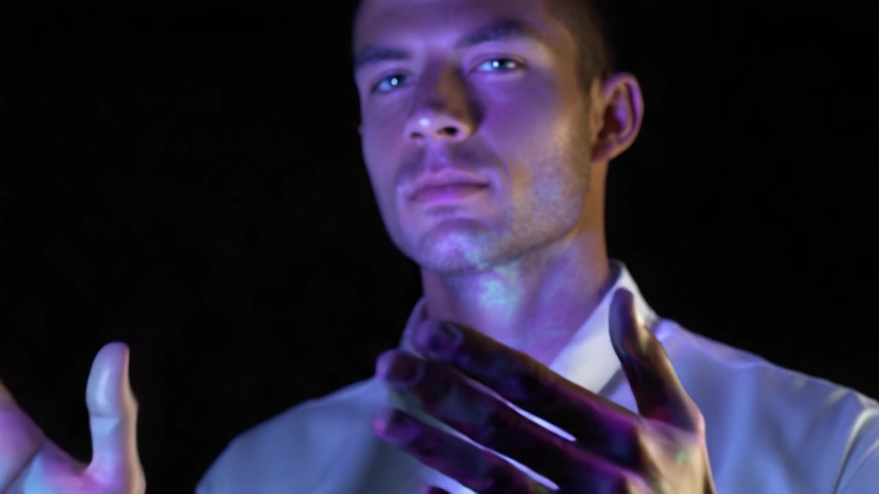 A man showcases his hands illuminated with colorful light patterns, reflecting a blend of art and science in an engaging visual display against a dark background.