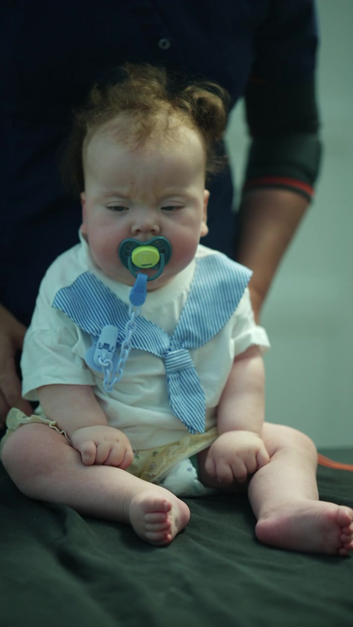 Cute infant with curly hair and blue eyes, wearing a bow tie and pacifier, looking up. Celebrating childhood innocence