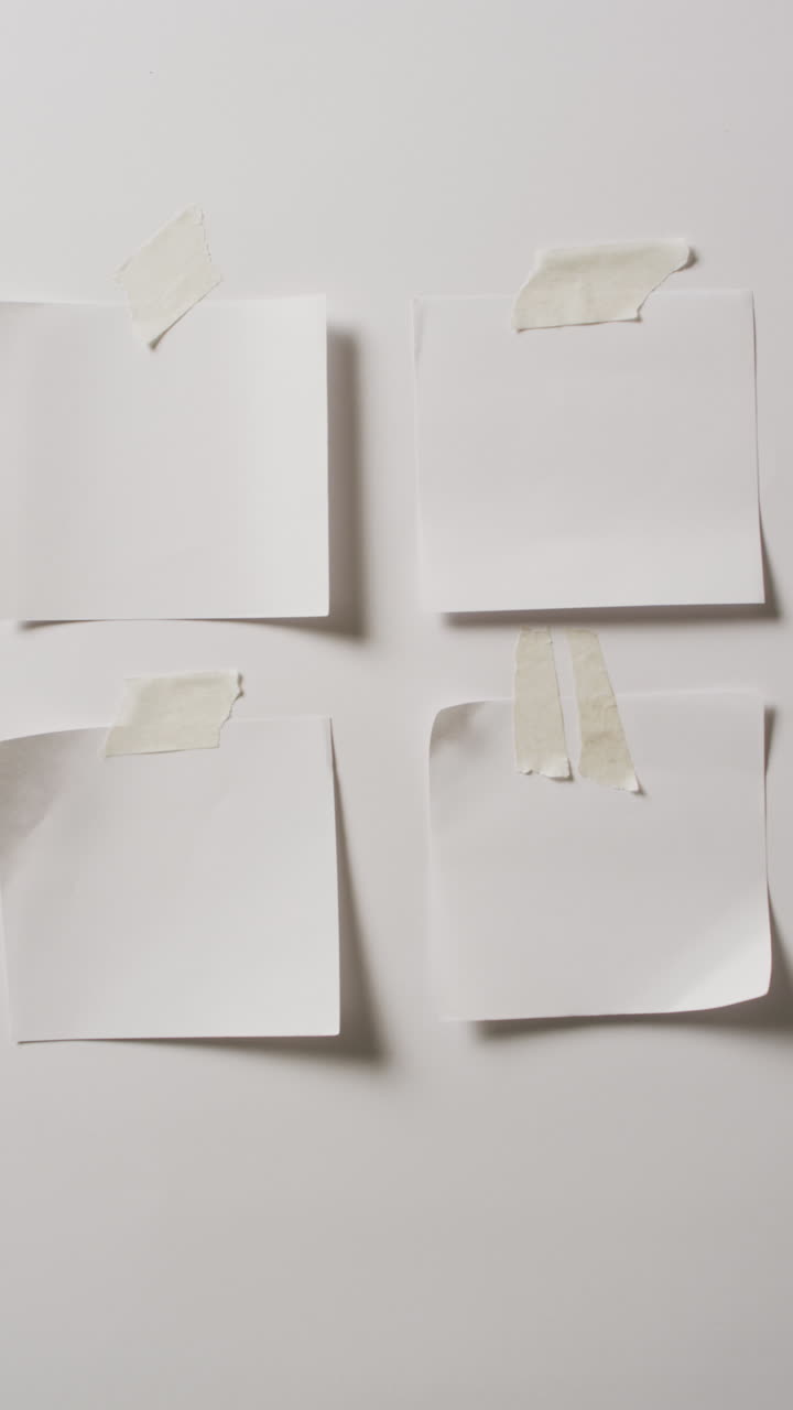 Vertical video of close up of four white memo notes taped to white background with copy space