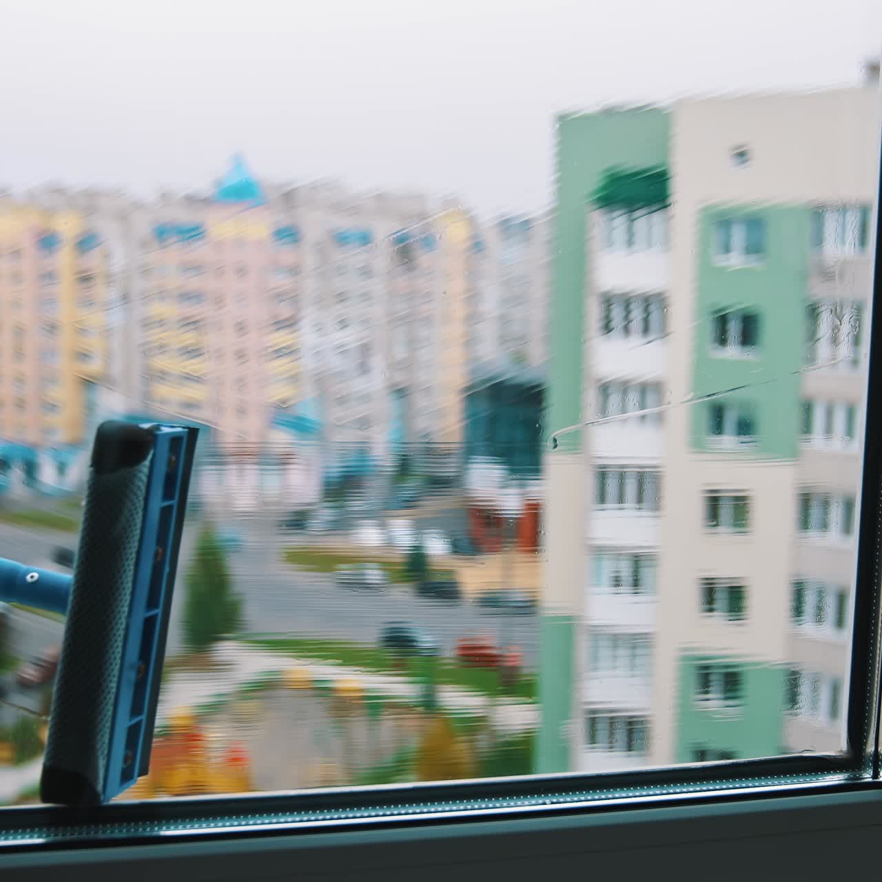 Washing window in the city flat. Man worker cleaning window with a special brush using water on the city background