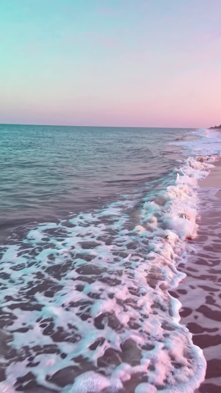 Aerial view of a serene beach at sunset, capturing gentle waves and a pastel sky