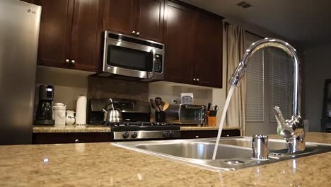 tracking shot, inside a home kitchen, water running at faucet, appliances in background, in california, usa