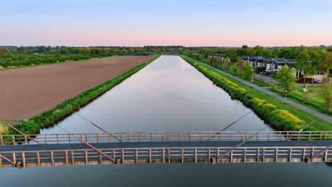 bridge over calm water, netherlands. sunset casts a warm glow on the bridge spanning a serene canal, surrounded by lush greenery and fields