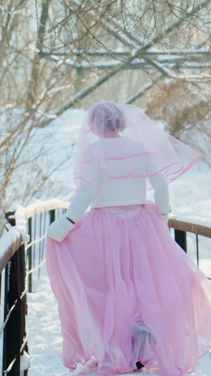 Sposa stravagante in abito rosa che corre su un ponte invernale innevato