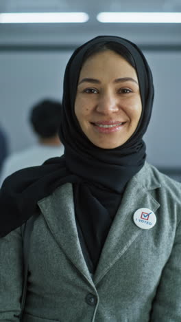 Portrait-of-mature-woman,-United-States-of-America-elections-voter.-Businesswoman-stands-in-a-modern-polling-station,-poses-and-looks-at-camera.-Background-with-voting-booths.-Concept-of-civic-duty.