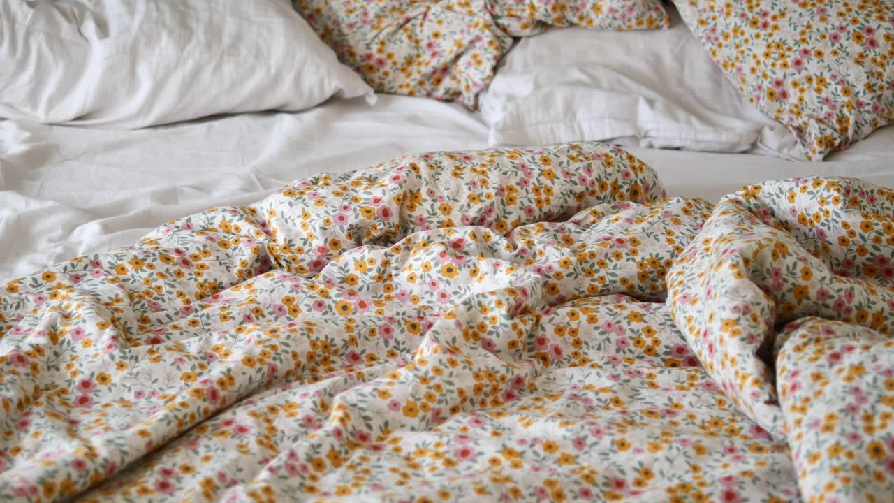 Cama deshecha con edredón floral y sábanas blancas