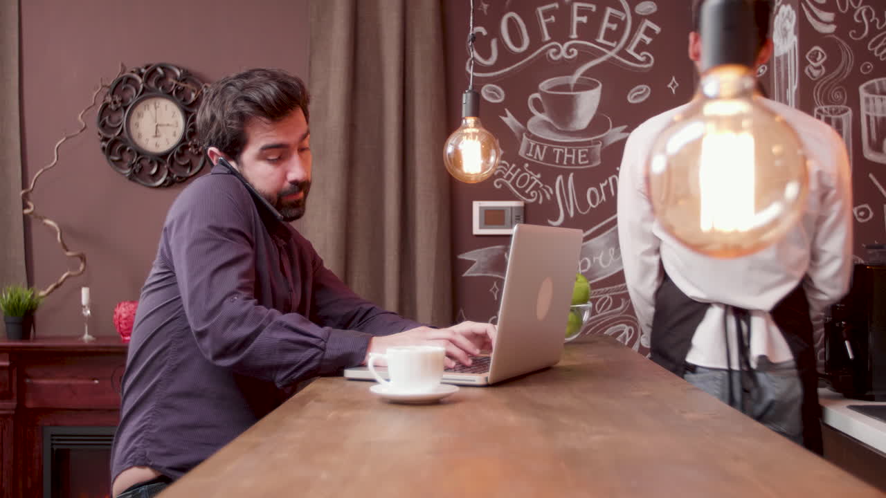 Man on phone and using laptop in a cafe