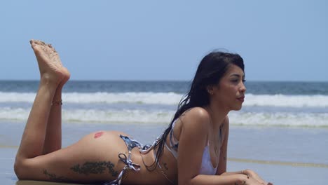 a bikini-clad latina girl soaks in the sun on a beautiful day at a caribbean beach laying on the white sand