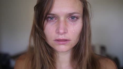 a close up, portrait shot of a young woman with wounds and bruises, looks and stares directly into the camera while a single tear is falling down from her eye onto her cheek and face