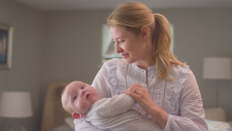 Loving-mother-carrying-and-cuddling-baby-son-in-bedroom-at-home---shot-in-slow-motion