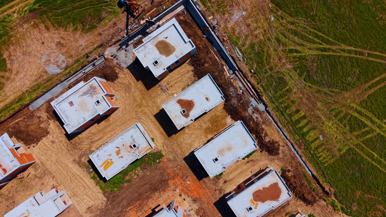 Vista aerea dall'alto di case residenziali in costruzione in un cantiere. Edifici incompiuti in mattoni e cemento in un cantiere con strade sterrate.