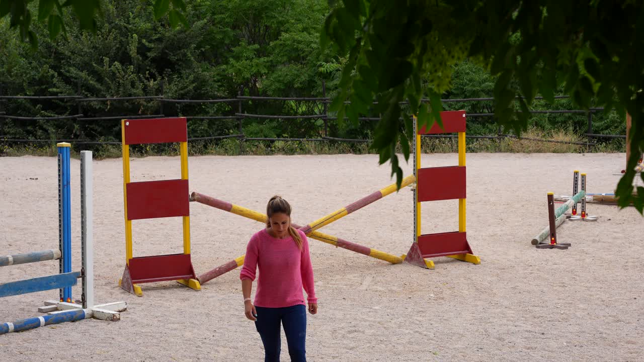 Female horse riding trainer leaving track after placing show jumping obstacles
